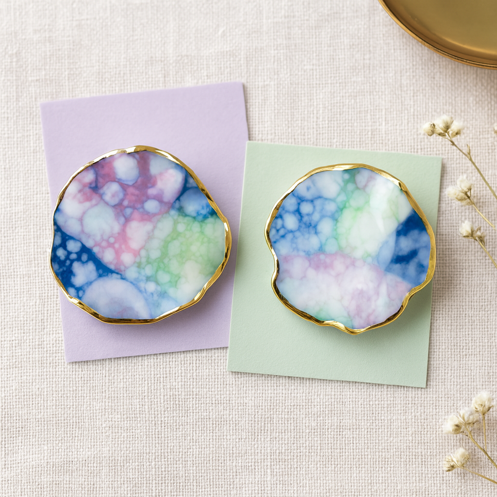 Pair of earrings with a multicolored marbled design and a gold border on a textured surface.