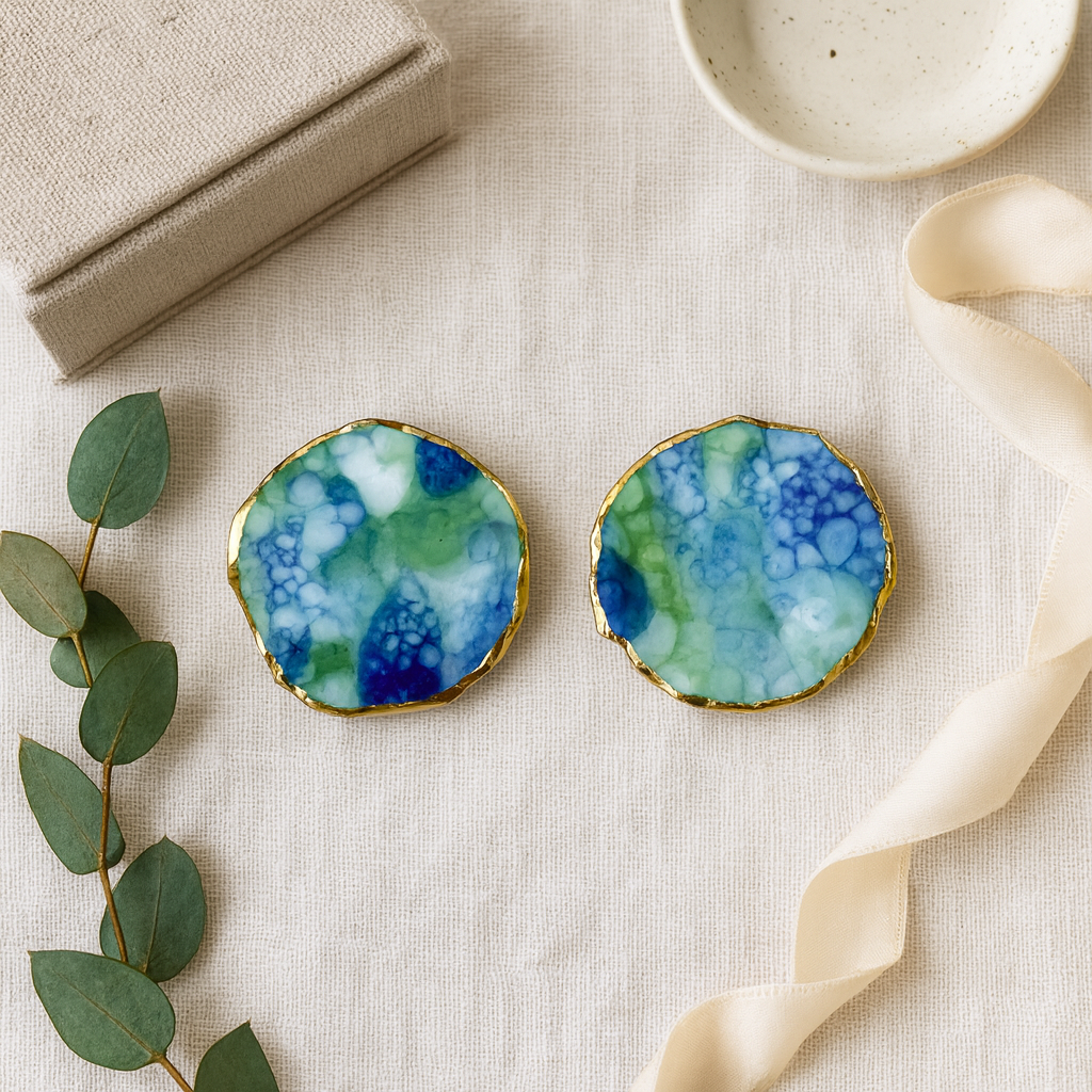 Round earrings with a blue and green marbled design on a beige fabric background.