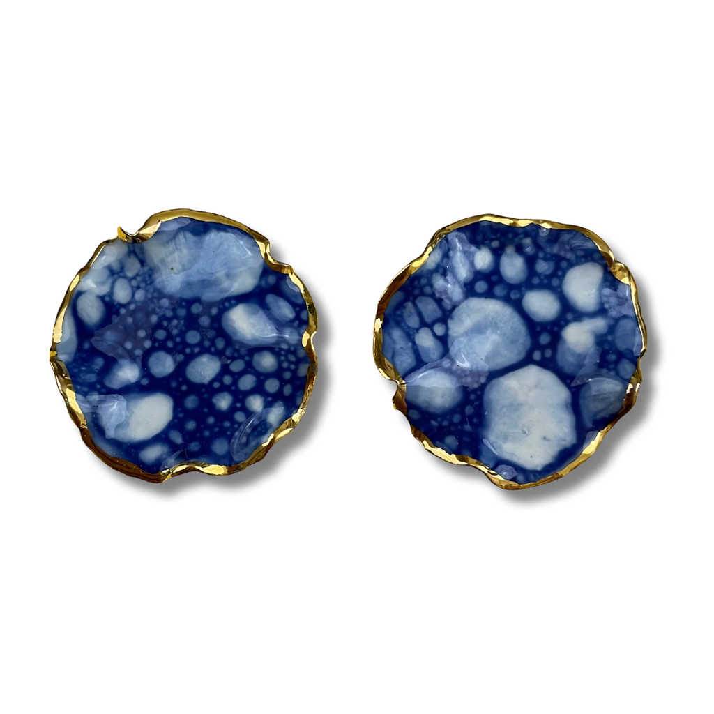 Pair of round earrings with a blue and white marbled design and a gold border against a white background