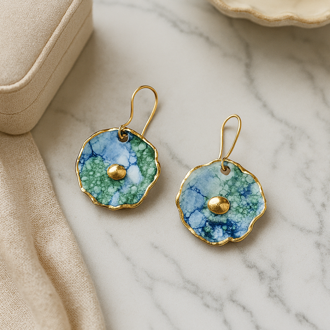 Pair of earrings with a green and blue design and gold details on a marble surface
