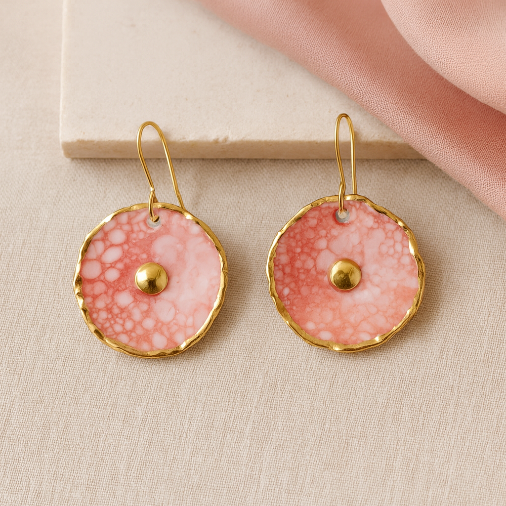 Pair of pink earrings with gold accents on a beige surface