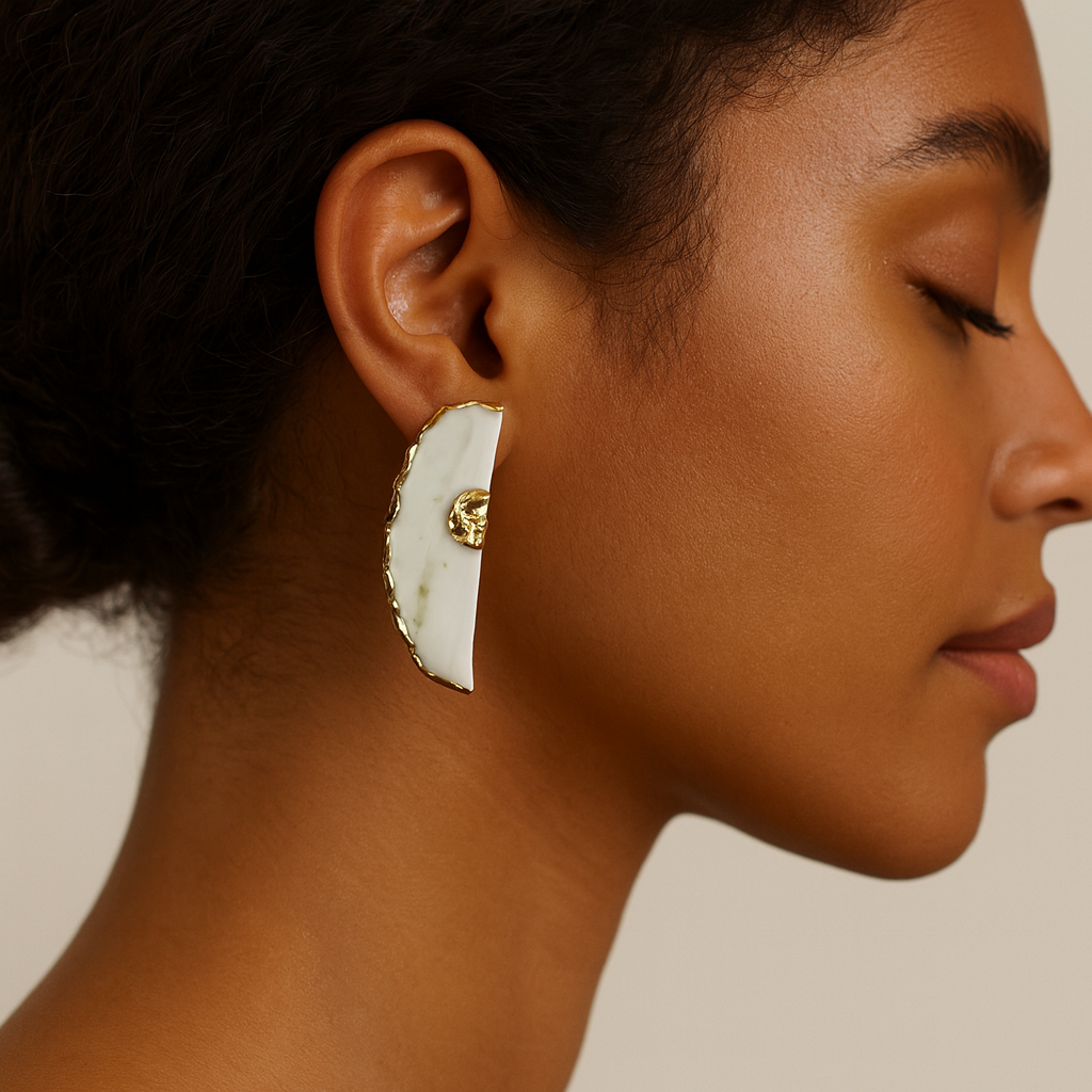 Close-up of a person wearing a gold and white earring on a neutral background