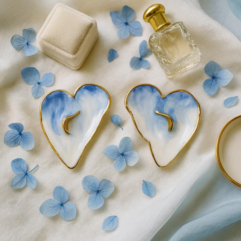 Heart-shaped earrings with a blue and white design and gold edges, surrounded by blue flowers on a light background