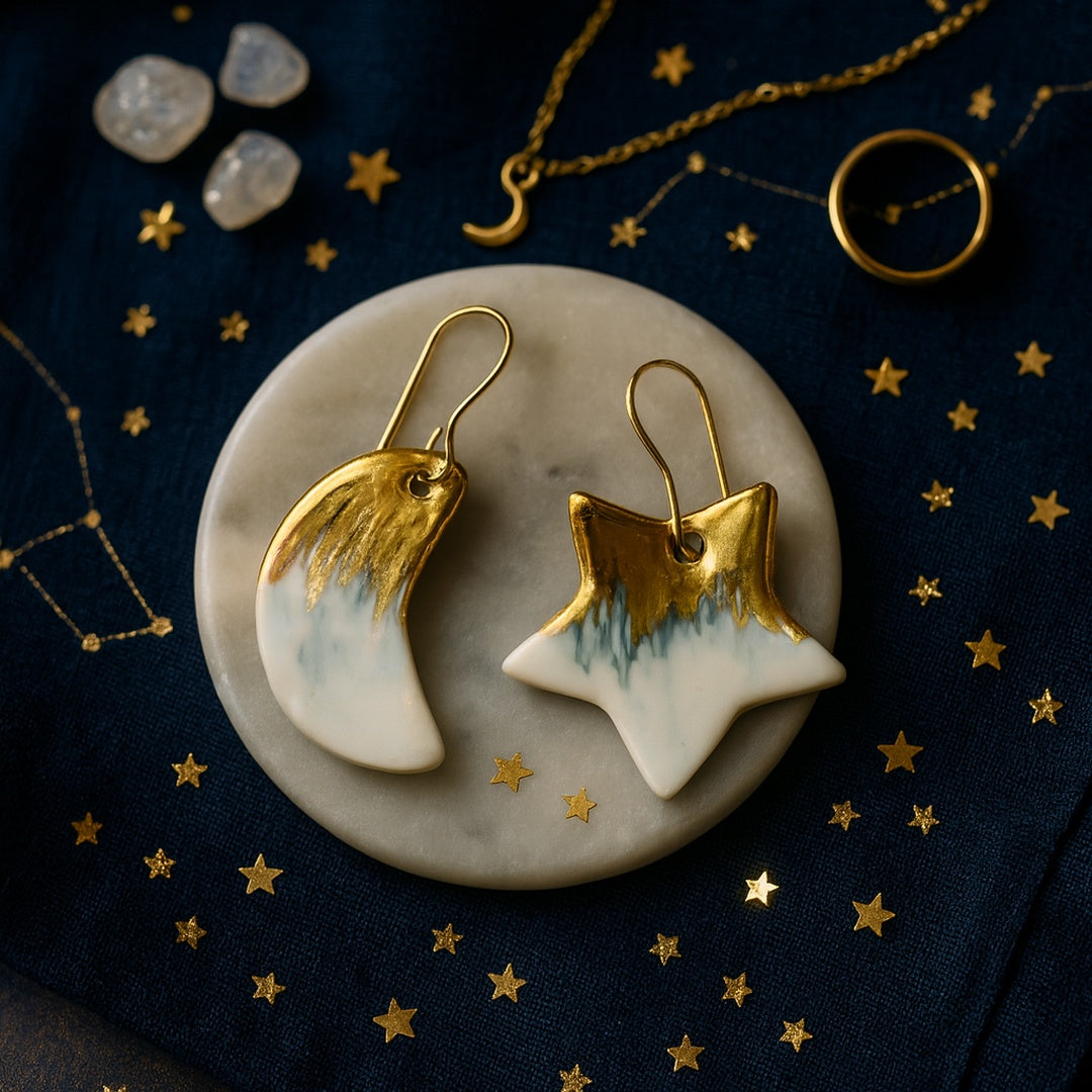 White and gold star and moon earrings on a dark blue background