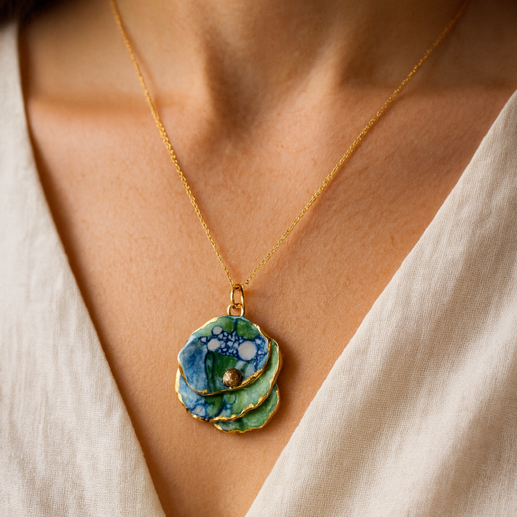 A multicolored porcelain pendant with gold accents on a person wearing a white top.